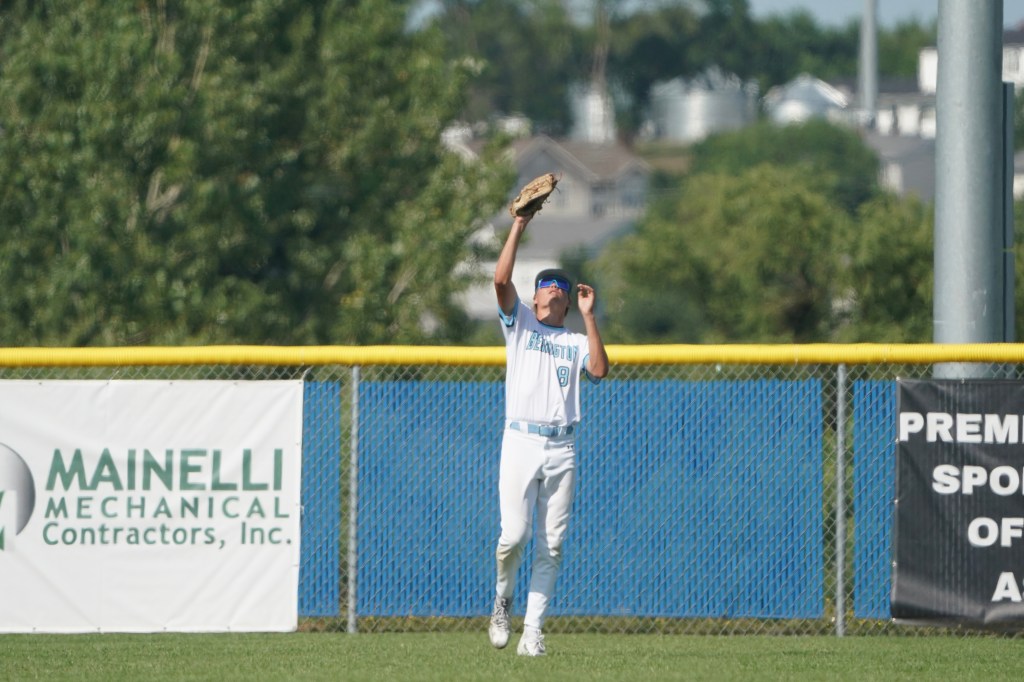 A baseball player wearing a blue jersey and white pants catching a fly ball in the outfield.