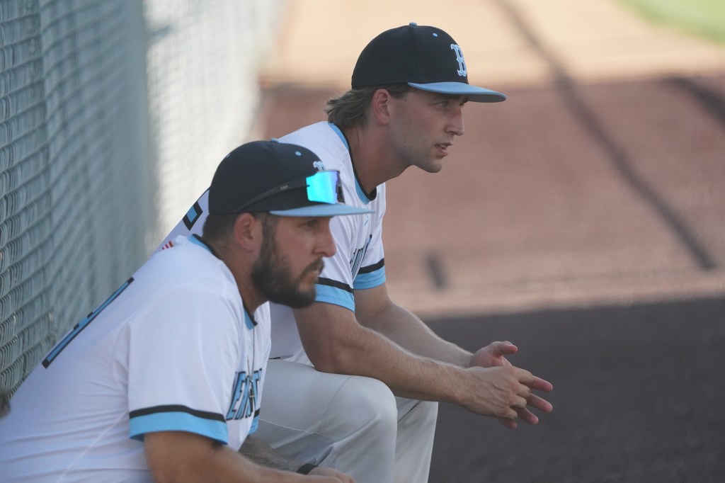 Two baseball players sitting on the bench, deep in thought, wearing team uniforms and caps.