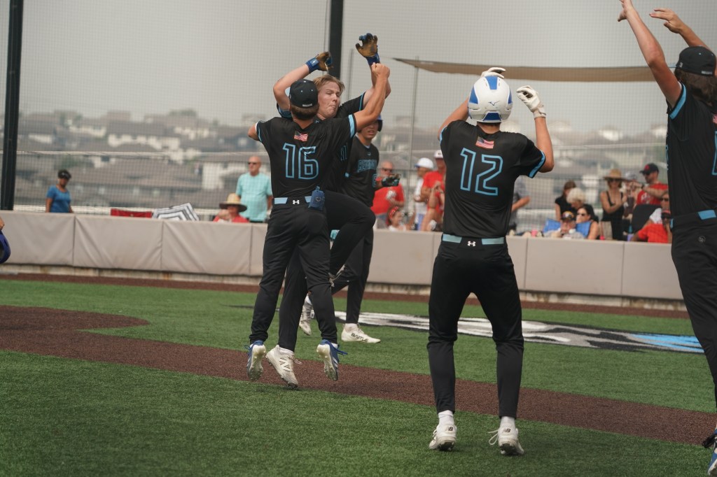A group of young baseball players celebrating a victory on the field, with one player jumping and others raising their arms in excitement.