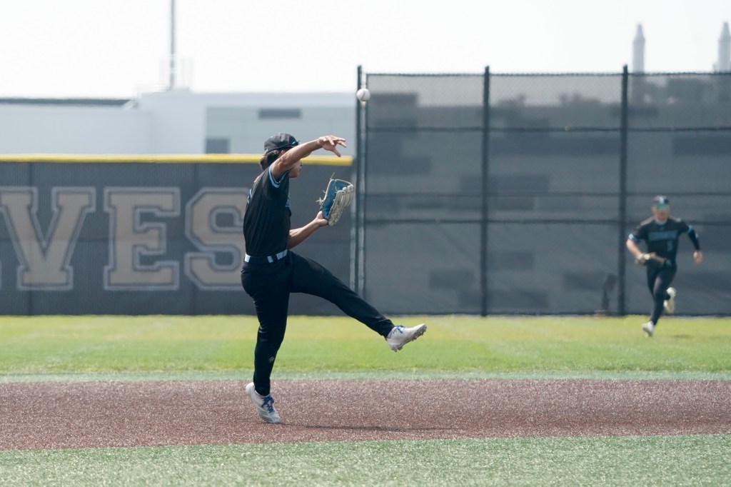 A baseball player preparing to throw a ball while standing on the infield grass, with a teammate visible in the background.