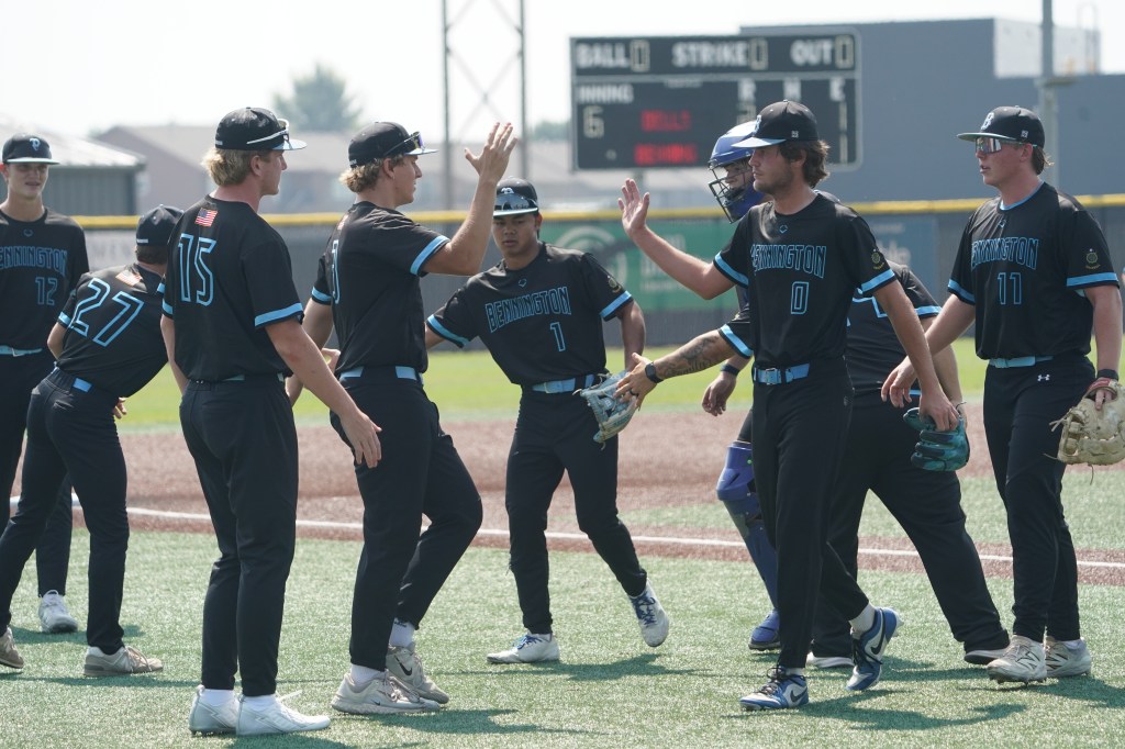 A group of baseball players in black uniforms with blue accents high-fiving each other on the field, celebrating a play during a game.