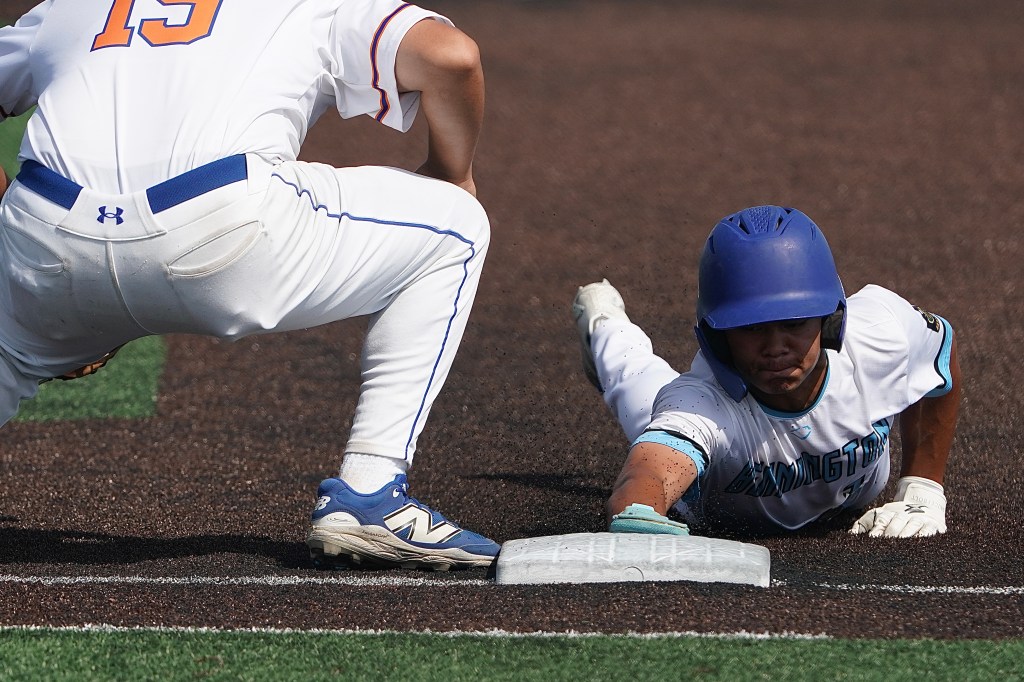 A baseball player sliding into a base while another player is in a crouched position nearby. The player in white is reaching for the base, demonstrating a dynamic play on the field.