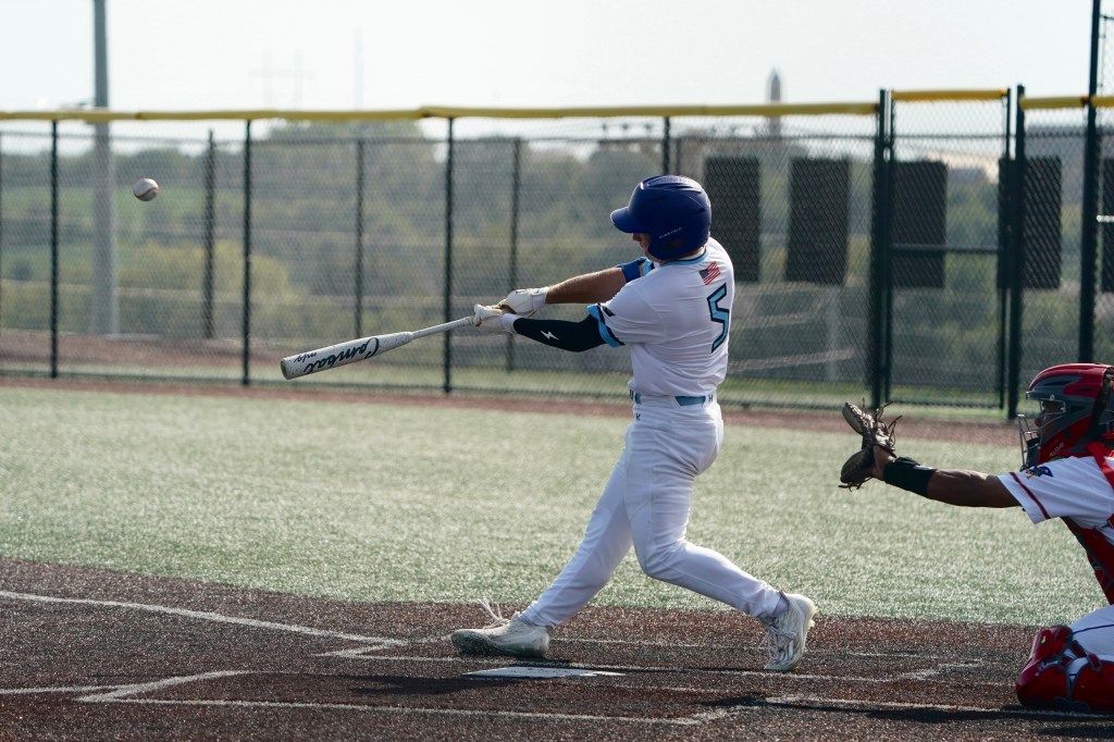 A young baseball player swings a bat at a pitched ball while a catcher waits behind home plate.