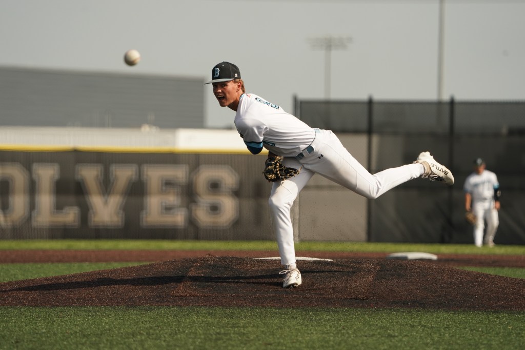 A baseball pitcher in a white uniform is throwing a pitch on a sunny day, with another player visible in the background.