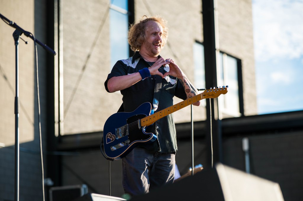 Musician on stage makes a heart shape with hands while holding a guitar.