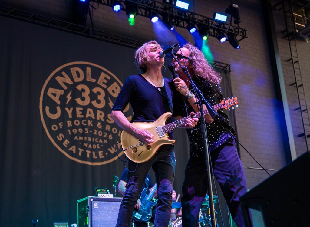 Two musicians perform on stage with a guitar, singing closely into a microphone, in front of a backdrop celebrating 'Candlebox 33 Years of Rock & Roll'.