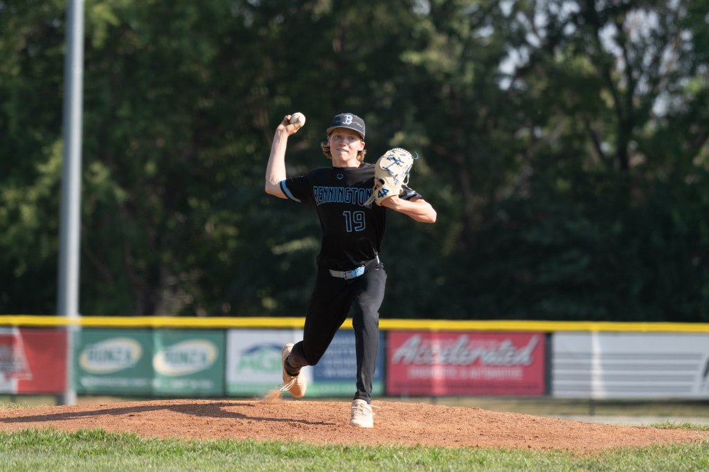 A young baseball pitcher in a black jersey, number 19, preparing to throw a pitch on the mound.