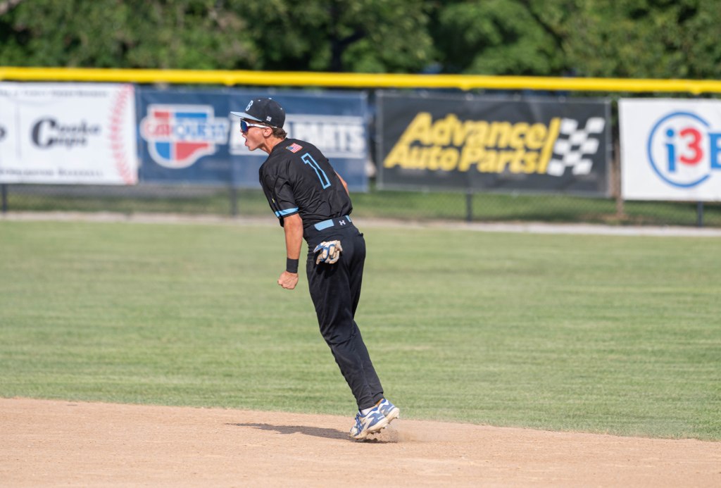 A baseball player in a black uniform, number 1, is celebrating or reacting on the field, with a focused expression and raised arm, against a backdrop of advertising banners.