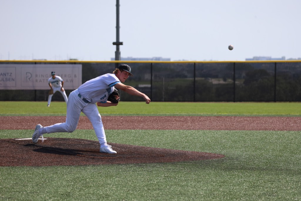 A pitcher throwing a baseball from the pitcher's mound in a baseball game. Another player is positioned in the background, ready to field the ball.