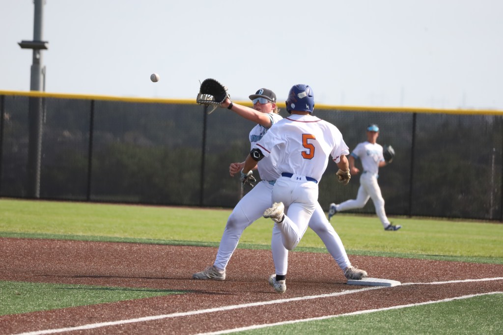 A baseball player attempting to catch a ball while another player runs toward first base during a game.