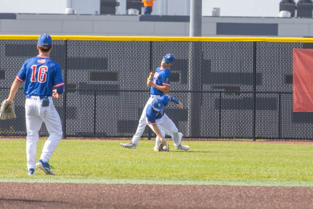 Baseball players in a field during a game, one player is catching a ball while another is falling in the grass.