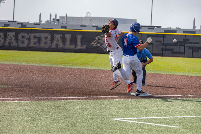 A baseball player in a white uniform catches a ball while another player in a blue uniform approaches first base, during a game.