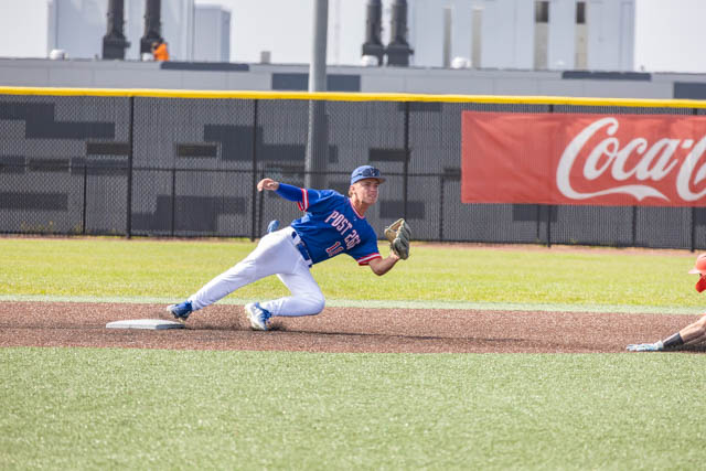 A baseball player in a blue jersey slides to catch a ball on the field, with a Coca-Cola advertisement in the background.