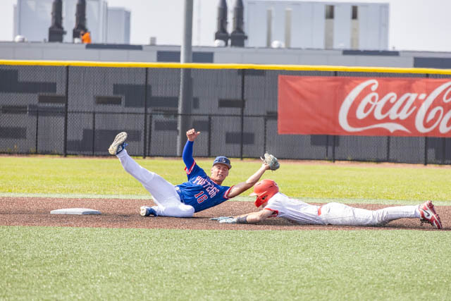 A baseball player in a blue uniform slides to second base, while a player in a white uniform stretches to tag him as he dives safely.