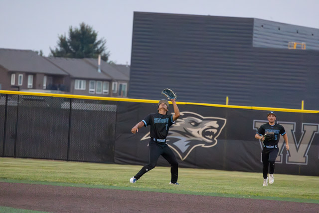 A baseball player catches a fly ball while another player stands nearby on the field.