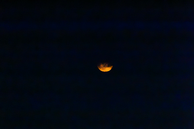 A partially illuminated orange moon against a dark night sky.
