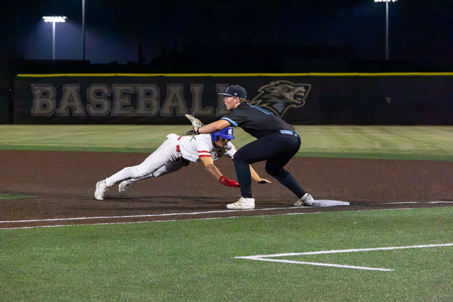 A baseball player sliding into first base as a fielder attempts to tag him during a night game.