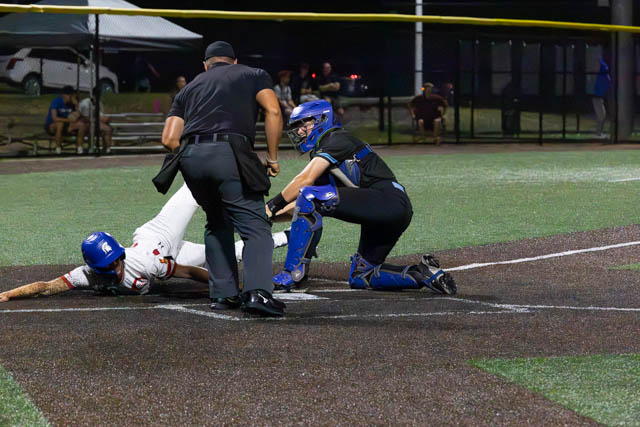 A baseball player sliding towards home plate, while the catcher prepares to make a play. An umpire is positioned nearby.