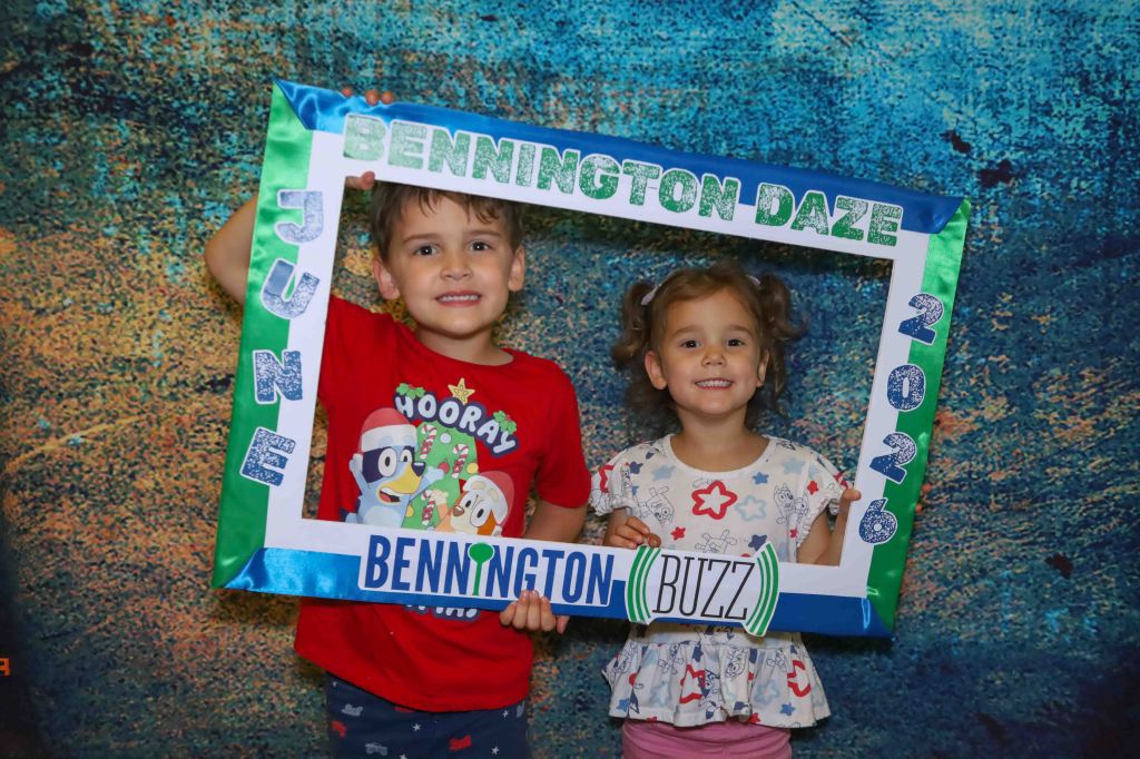 Two children posing with a colorful frame that reads 'Bennington Daze June 2026'. The boy is wearing a red shirt with cartoon characters, while the girl is in a white shirt with stars and airplanes.