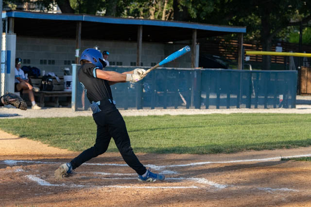 A player in a black uniform swings a blue baseball bat at a pitch on a baseball field.