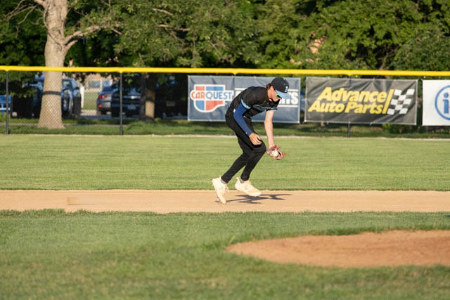 A young male baseball player is running on a field, preparing to field a ground ball near second base.