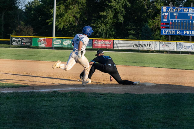 A baseball player in a blue uniform is sliding towards a base while a player in a black uniform attempts to tag him out during a game.