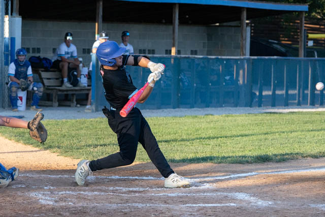 A baseball player in a black uniform swings a pink bat while batting at home plate, with teammates in the background.