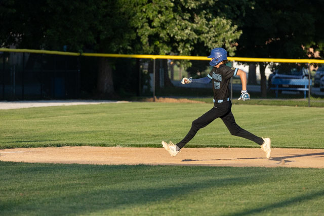 A young baseball player running on the field, wearing a black uniform and blue helmet, with a focus on their dynamic movement as they approach home plate.
