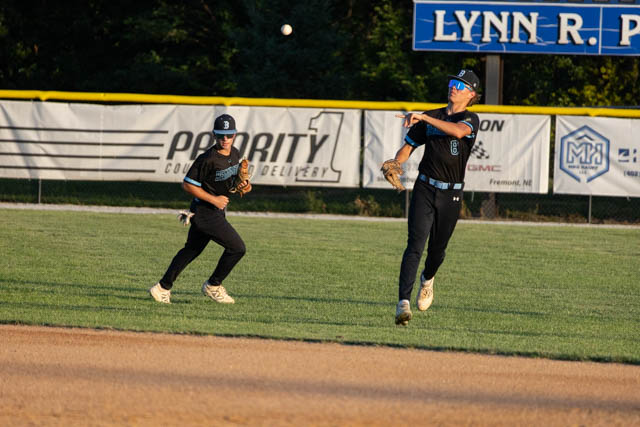 Two young baseball players on a field; one is catching a fly ball, while the other is positioned nearby, ready to assist.
