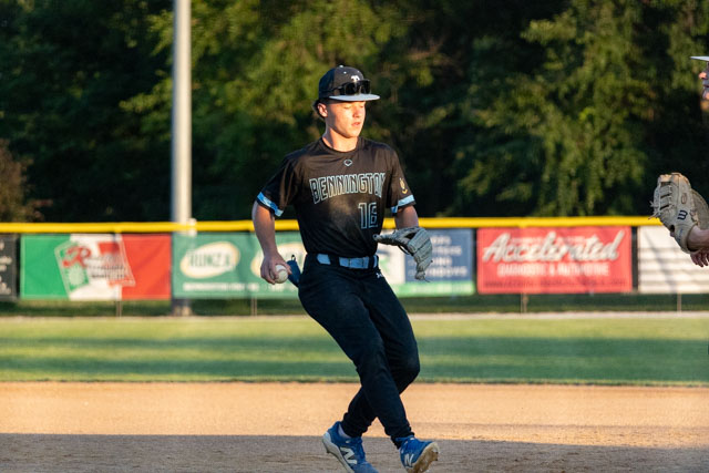 A youth baseball player in a black jersey numbered 16, running on a baseball field with a focused expression.