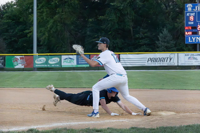 A baseball player in a white uniform with the number 17 is making a play at first base, while a sliding player in a black uniform attempts to avoid being tagged out.
