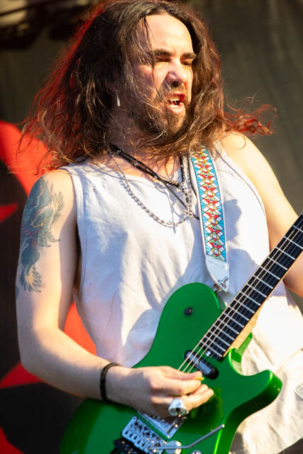 A musician with long hair passionately playing a bright green electric guitar on stage.