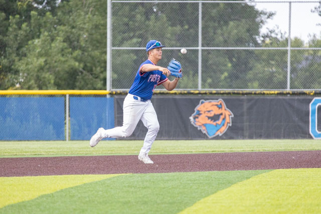 A baseball player in mid-air catching a ball while playing on a field, wearing a blue jersey and white pants.