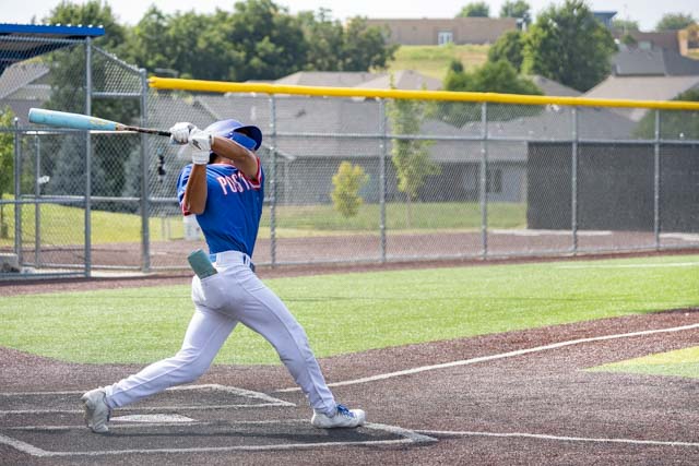 A young baseball player in a blue jersey swings a bat during practice on a well-maintained field.