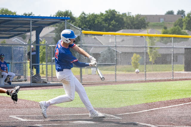 A young baseball player in a blue jersey swings a bat at a baseball during a game on a sunny day.