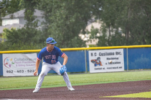 A baseball player in action, crouching on the field with a glove, wearing a blue jersey and white pants.
