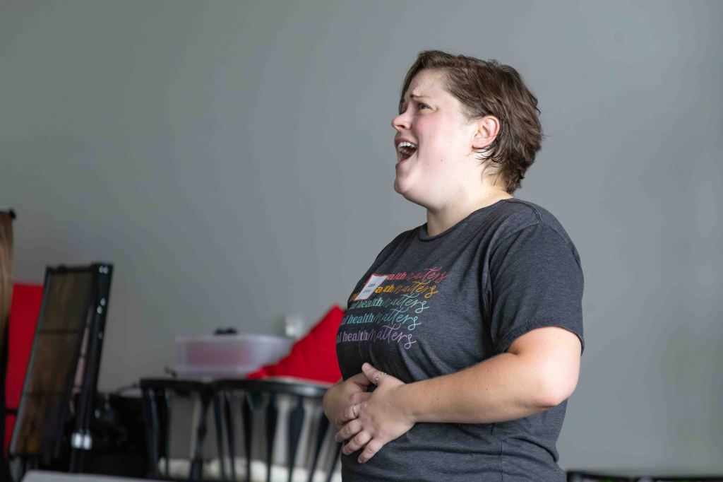 A woman passionately singing or performing, with a focused expression, in a casual setting.