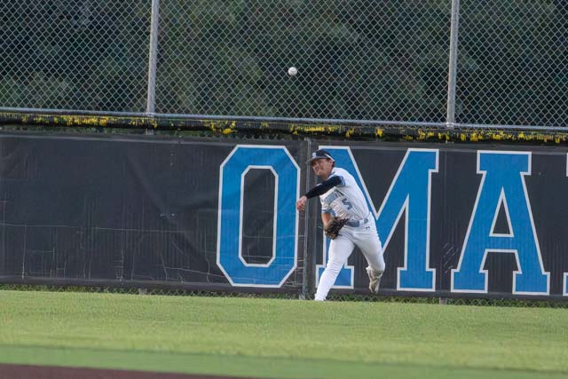 A baseball player in a white uniform catches a fly ball near the outfield fence, with the word 'OMAHA' displayed on the wall behind him.