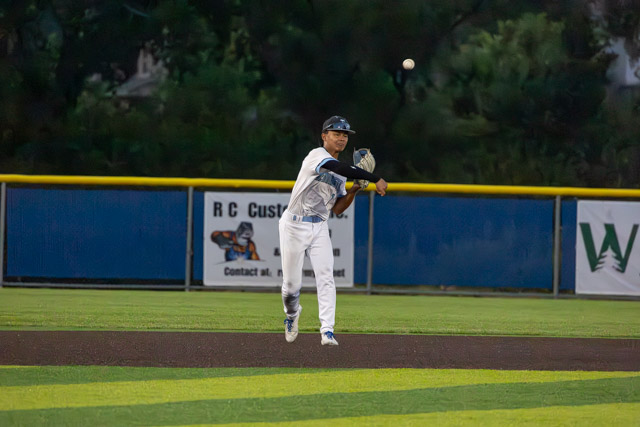 A baseball player in a white uniform makes a throw to a teammate while fielding the ball on a baseball field.