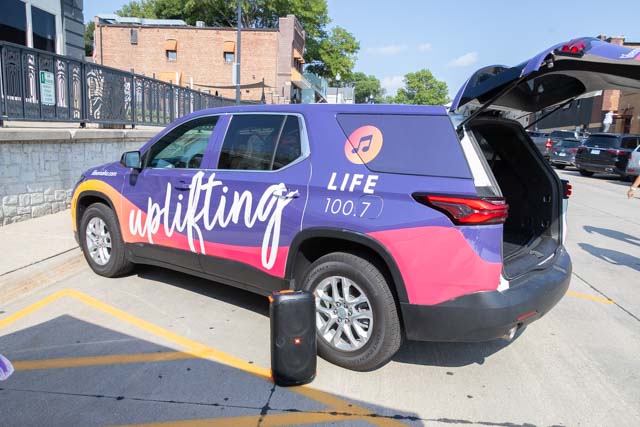 A parked vehicle with a colorful advertisement promoting 'Life 100.7' and the word 'uplifting' displayed prominently on its side.