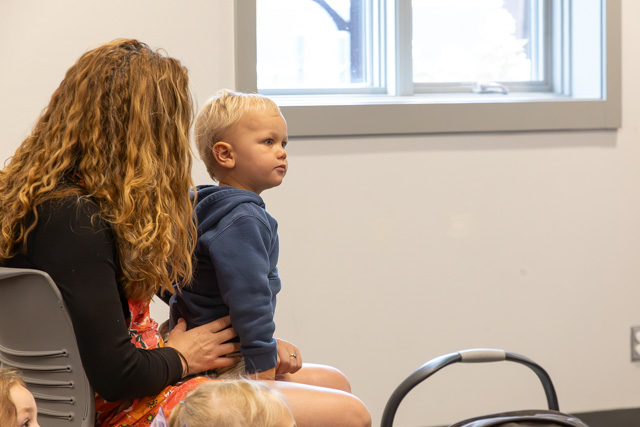 A child sitting on a woman's lap, both looking towards a window in a classroom setting.