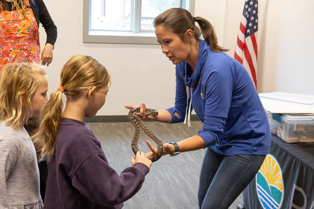 A teacher engaging with two children while holding a snake, demonstrating it as a part of an educational activity.