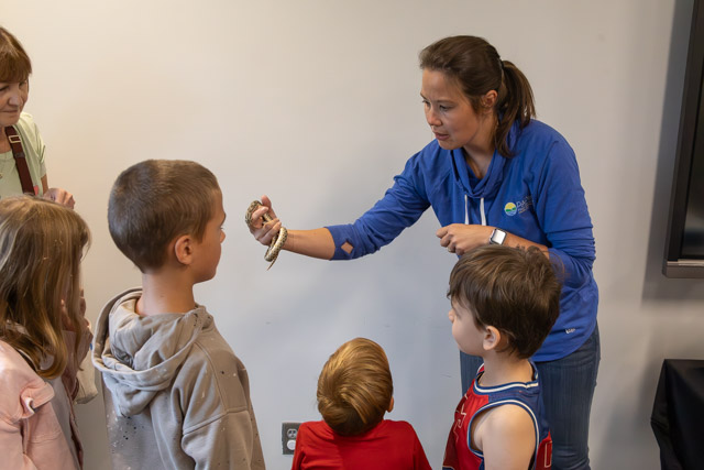 A woman shows a snake to a group of children during an educational presentation.