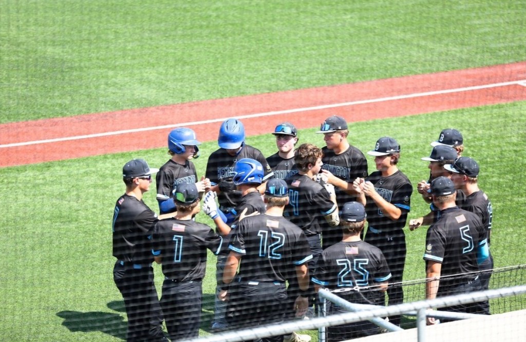 A group of young baseball players in black jerseys gathered on the field, discussing strategy or celebrating a moment during a game.