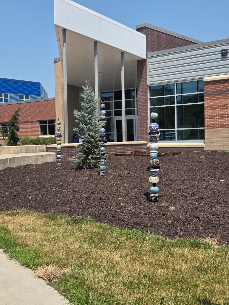 A modern building exterior featuring large glass windows, with decorative stacked stones in the foreground and a small evergreen tree.