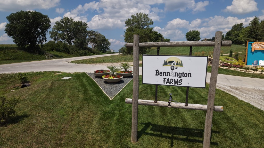 Sign for Bennington Farms located at a crossroads with green grass and decorative flower beds.