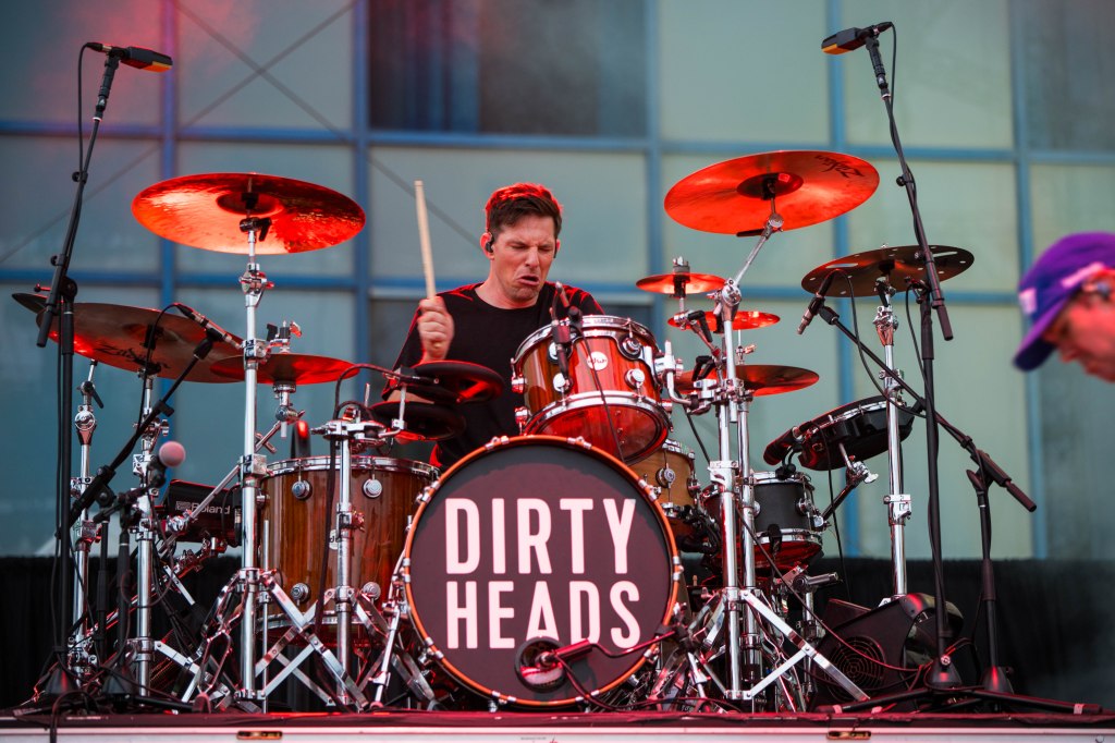 A drummer performing on stage with a drum set featuring the band name 'DIRTY HEADS' prominently displayed on the bass drum.