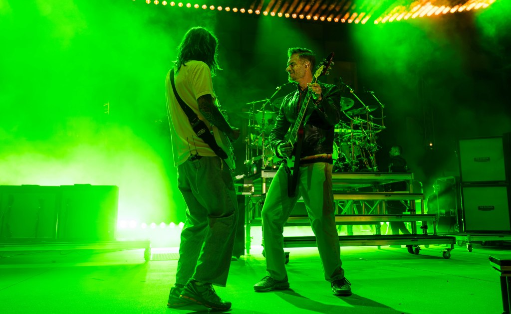 Two musicians performing on stage with a vibrant green fog and lighting.
