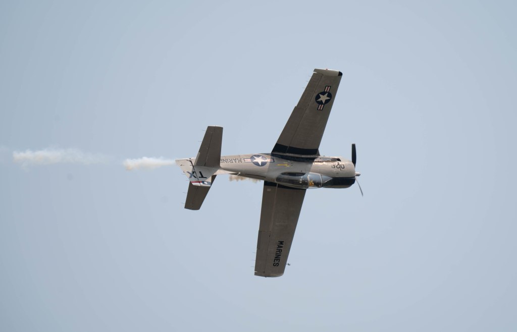 A military aircraft performing an aerial maneuver, emitting smoke trails against a clear blue sky.