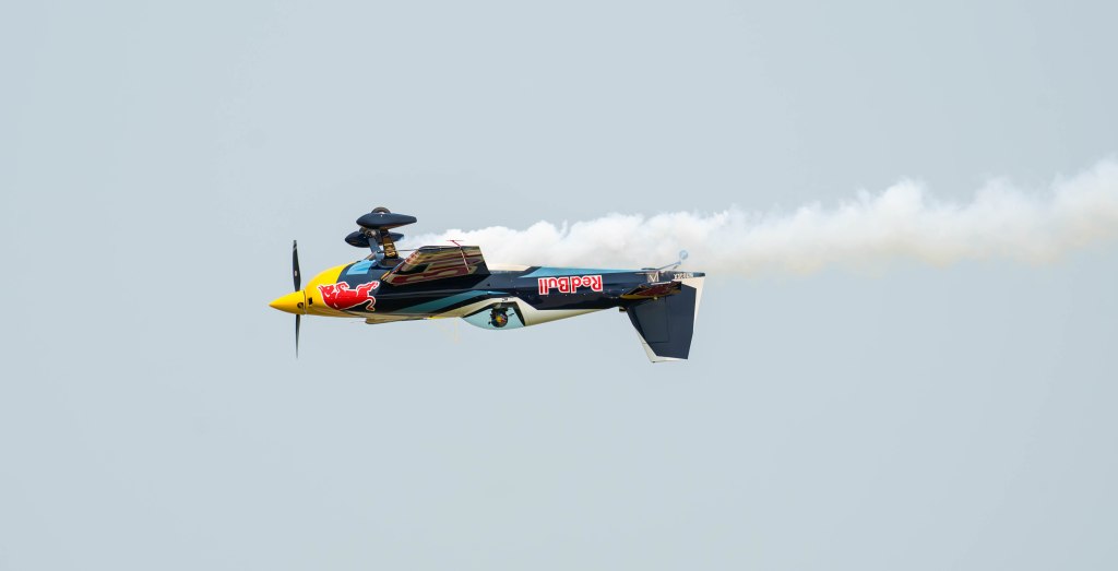 A stunt plane performing an aerial maneuver with smoke trailing behind it.
